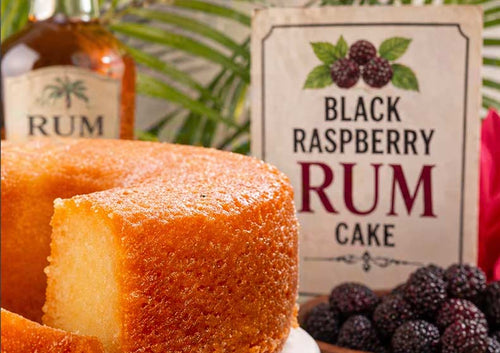 Black Raspberry Rum Cake with a bottle of rum and black raspberries in the background