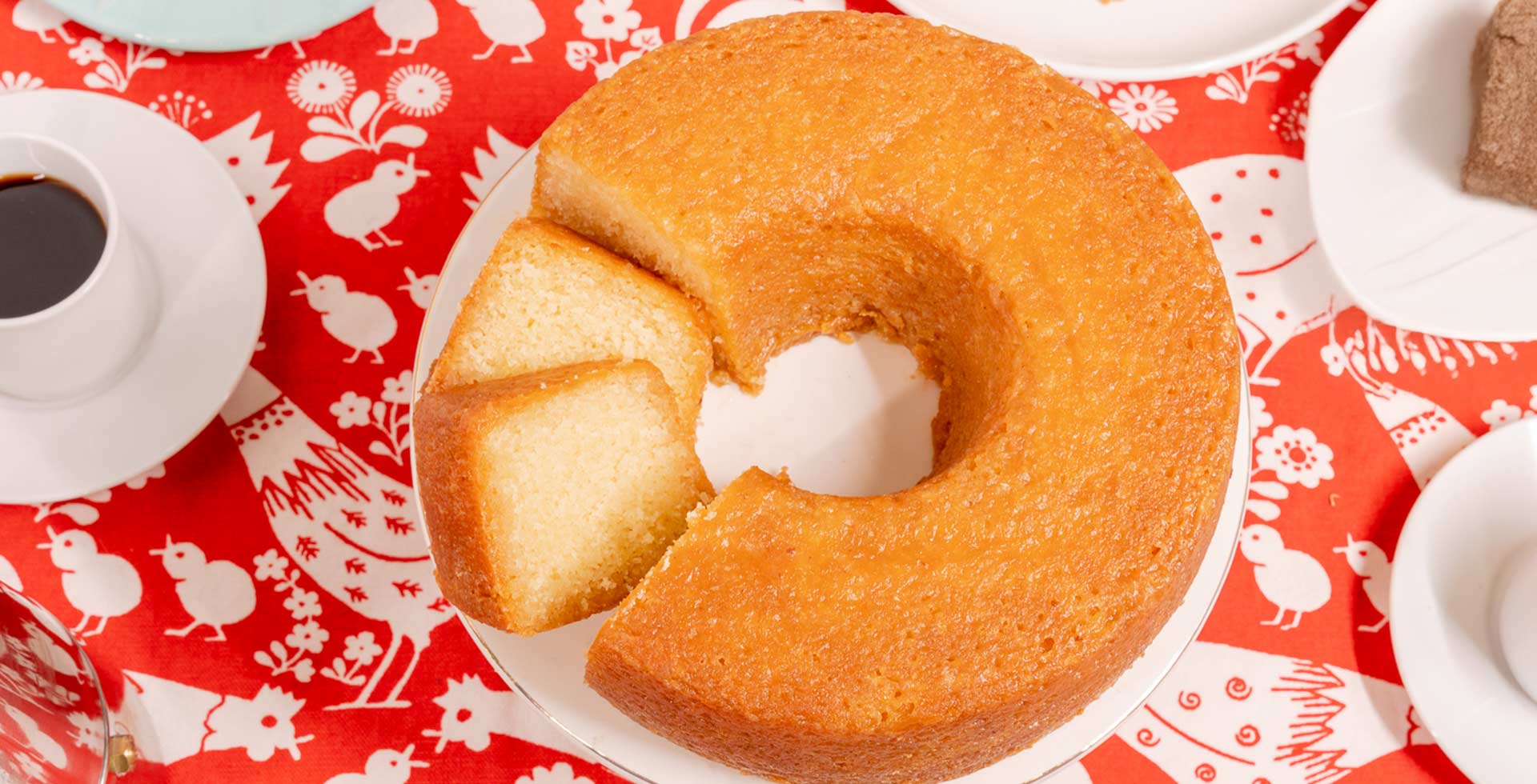 Round cake with a slice taken out on a decorative red and white tablecloth.