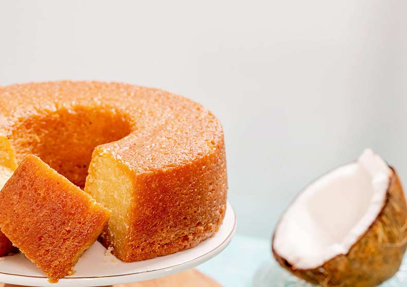 Coconut rum cake with a slice cut out on a white plate, next to a whole coconut.