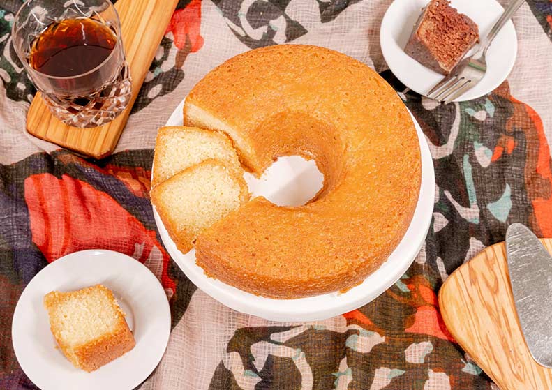 coconut butter rum cake on a white plate with a glass of coffee and a slice of cake on a plate in the background.