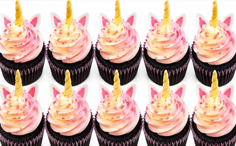 Unicorn-themed cupcakes with pink frosting and gold horns on a white background