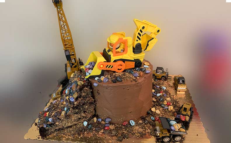 Construction-themed cake with toy excavator and crane on a gray background