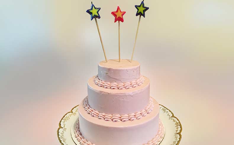 Three-tiered pink cake with star-shaped candles on a white background
