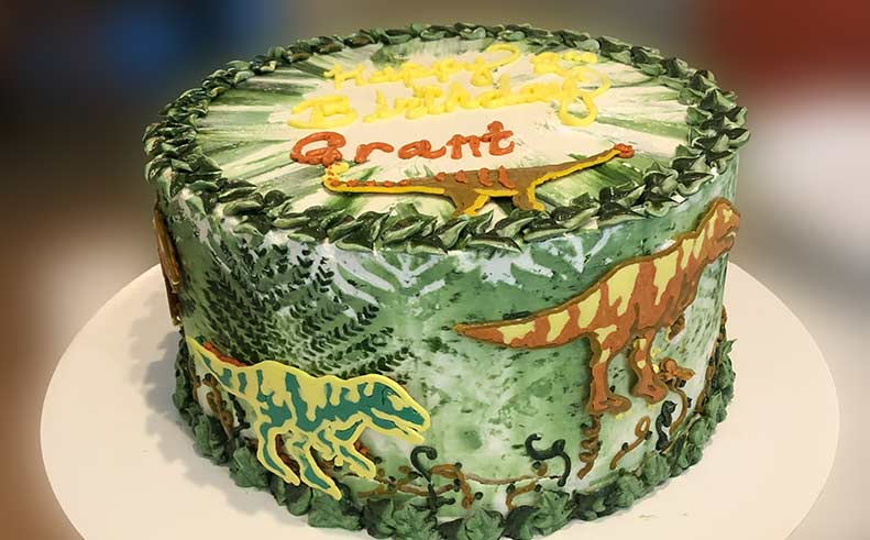 Dinosaur-themed birthday cake with 'Happy Birthday Grant' on a white plate.