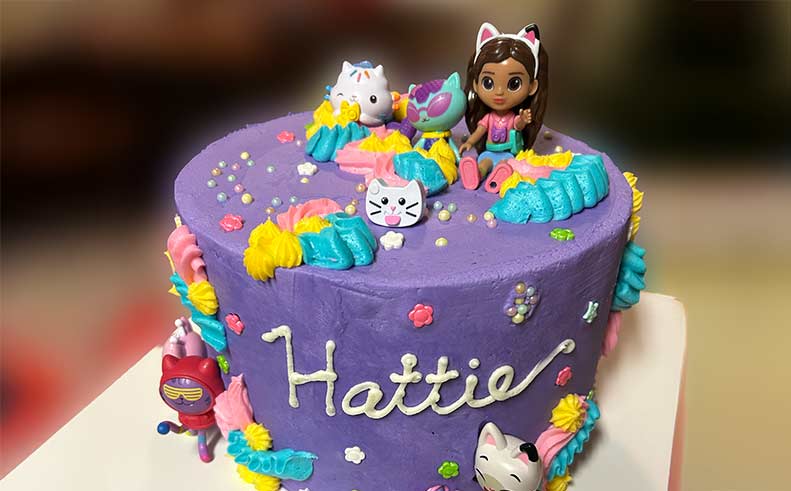 Decorative cake with colorful characters and 'Hattie' written on it.