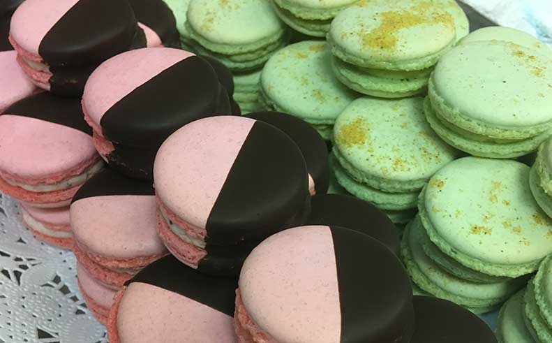 Macarons in pink, black, and green on a lace tablecloth.