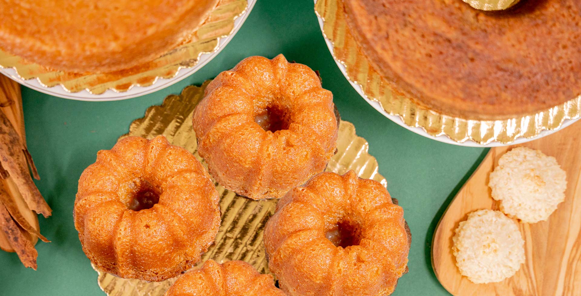 Small Bundt cakes on a green surface with a wooden board and cookies.