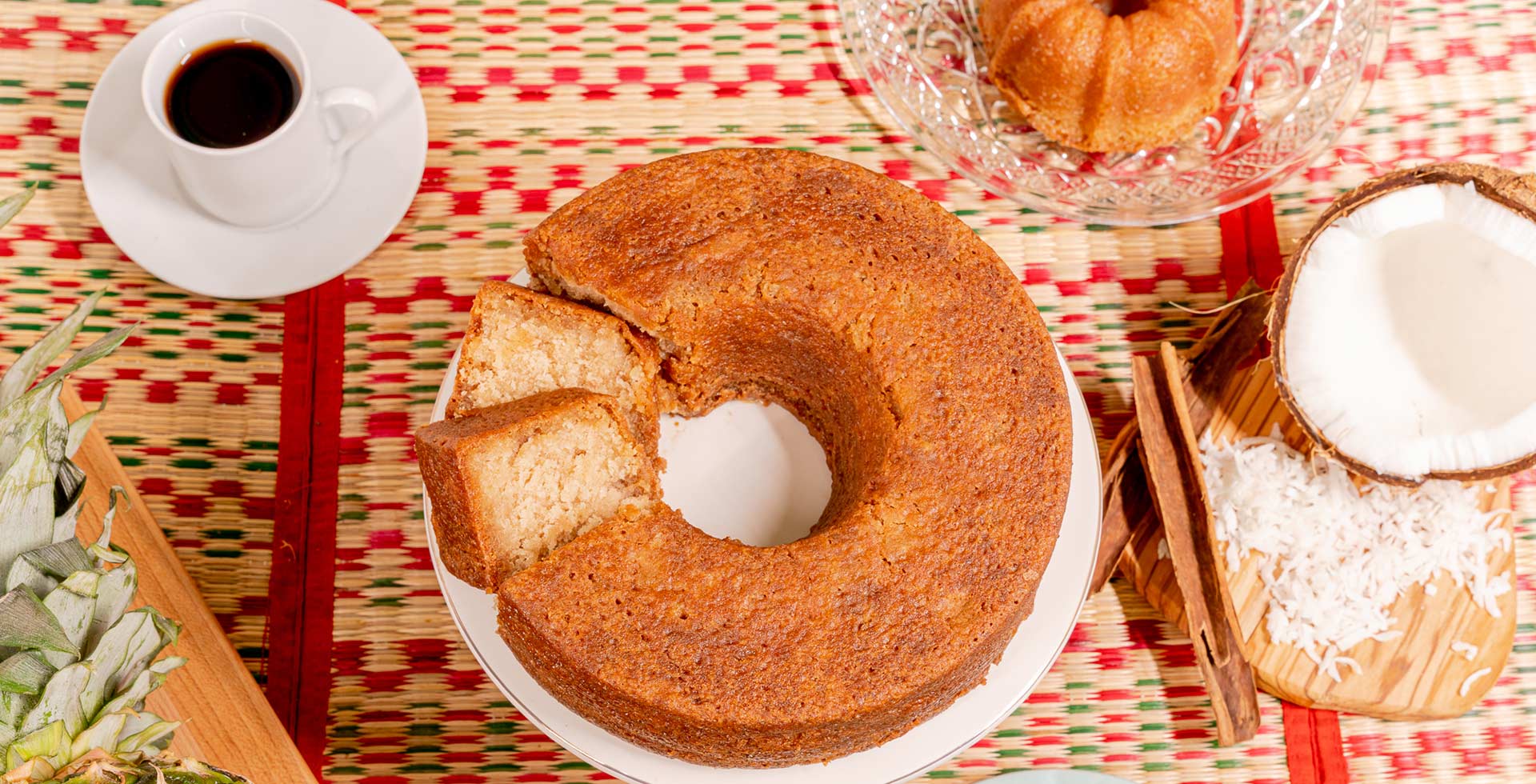Bundt cake on a plate with a cup of coffee and decorative items on a patterned tablecloth.