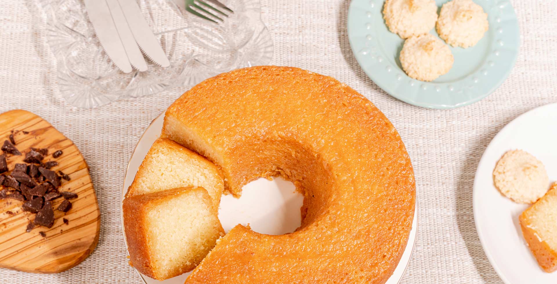 Bundt cake with cookies on a textured surface with plates of cake slices and chocolate pieces.