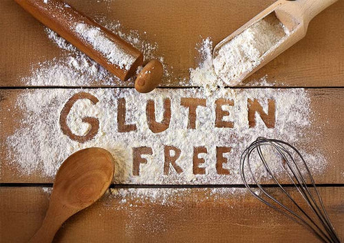 Wooden rolling pin, wooden spoon, and flour sifter on a wooden surface with 'GLUTEN FREE' text.