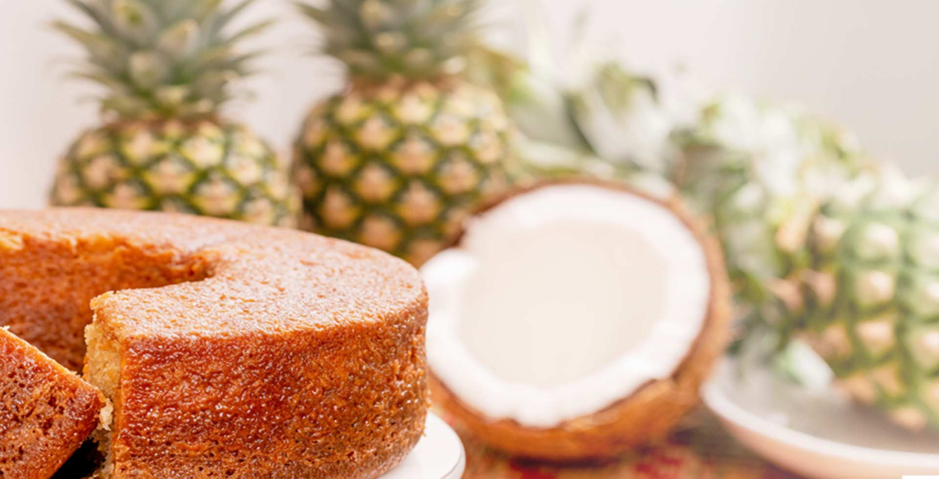 Sliced cake with a coconut on a decorative plate, surrounded by pineapples.