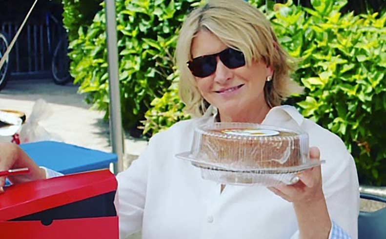 Martha Stewart holding a cake outdoors with sunglasses on 