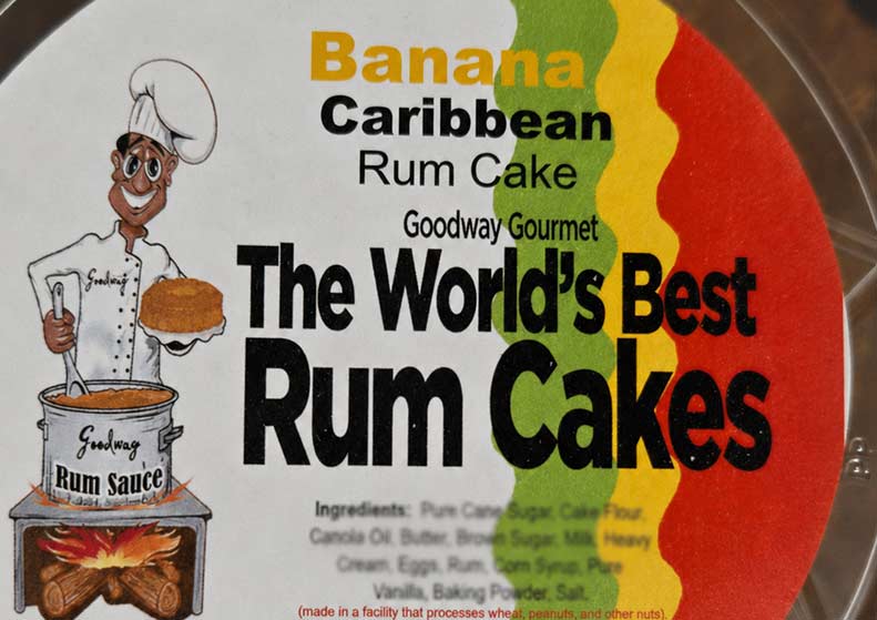 A close-up of a round food product package labeled 'Banana Caribbean Rum Cake' by Goodway Gourmet, with large text reading 'The World's Best Rum Cakes' and a cartoon chef holding a cake next to a pot of rum sauce.